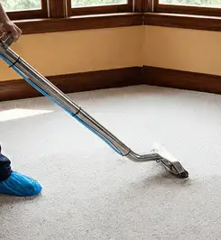 Steam carpet cleaning technician using a hot-water extraction wand on a residential carpet, wearing blue protective shoe covers Phoenix, AZ.