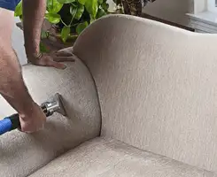 Professional upholstery cleaner deep-cleaning a fabric sofa with a handheld extraction tool and hose in Phoenix, AZ.